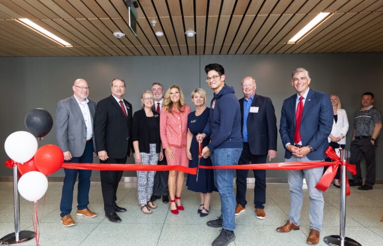 EWU leadership along with state representatives Joe Schmick, Leonard Christian, Suzanne Schmidt and Mary Dye pose with a student who has big scissors and is cutting the ribbon