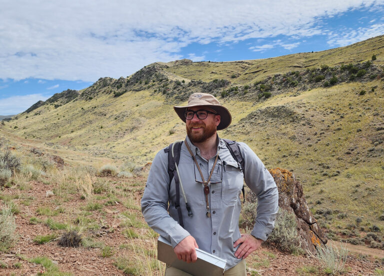Geosciences student stands atop a rocky hillside.