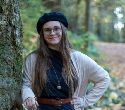Photo of McKenzie Riffner wearing a hat and leaning on a tree.