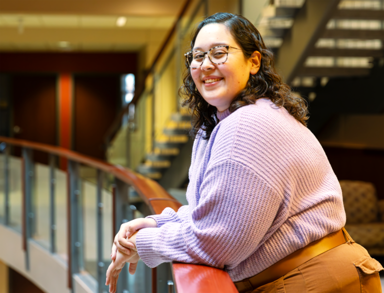 Photo of Madilyn Fisher leaning on a railing with stairs in the background.
